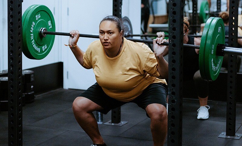 Body Fit Training studio member demonstrating a squat barbell workout