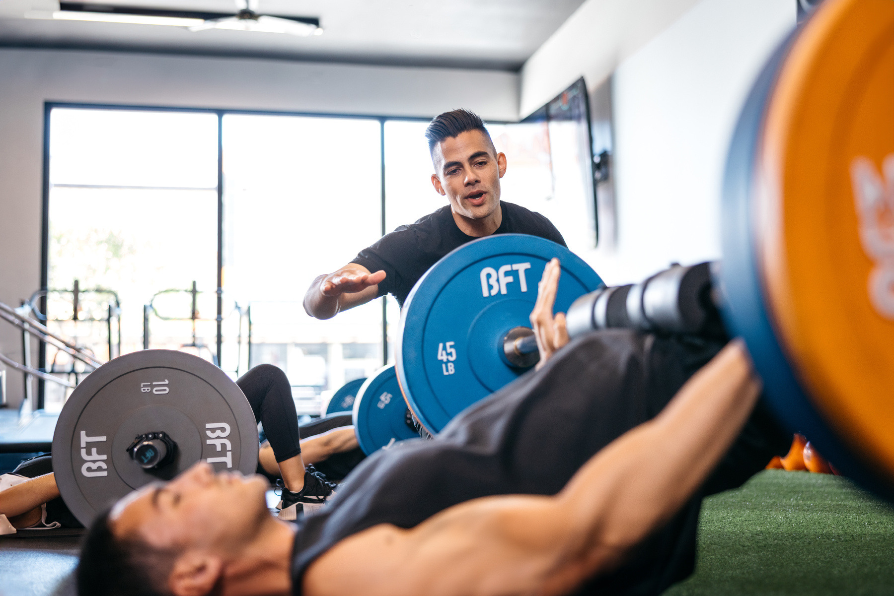 Group session attendees being guided by trainer on proper technique for hip thrust exercise