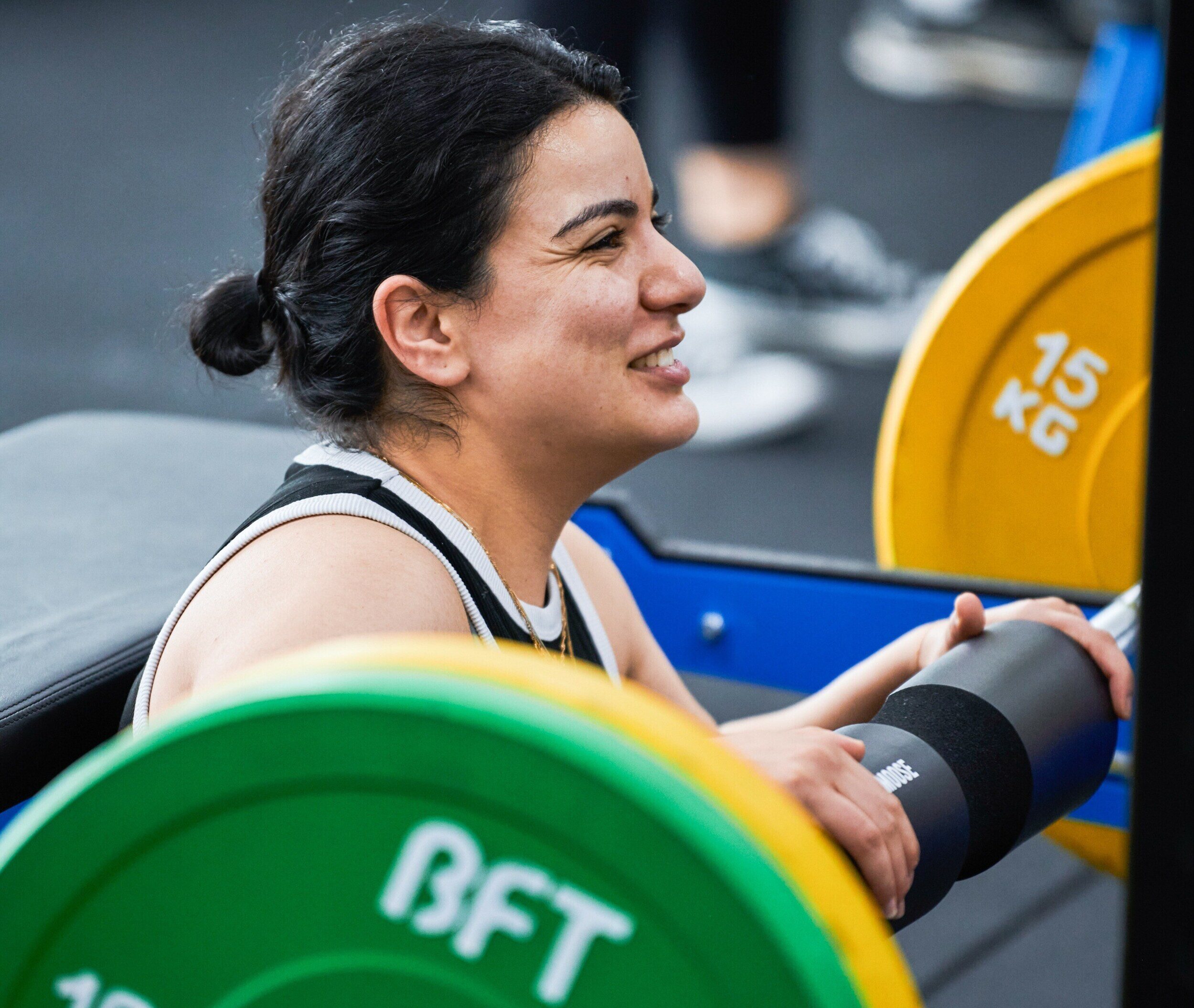 Weight Training session attendee smiling while receiving instructions from her trainer on benchpress machine