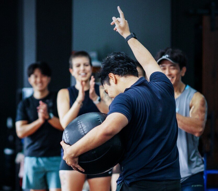 Body Fit Training group of attendees cheering on man holding a medicine ball