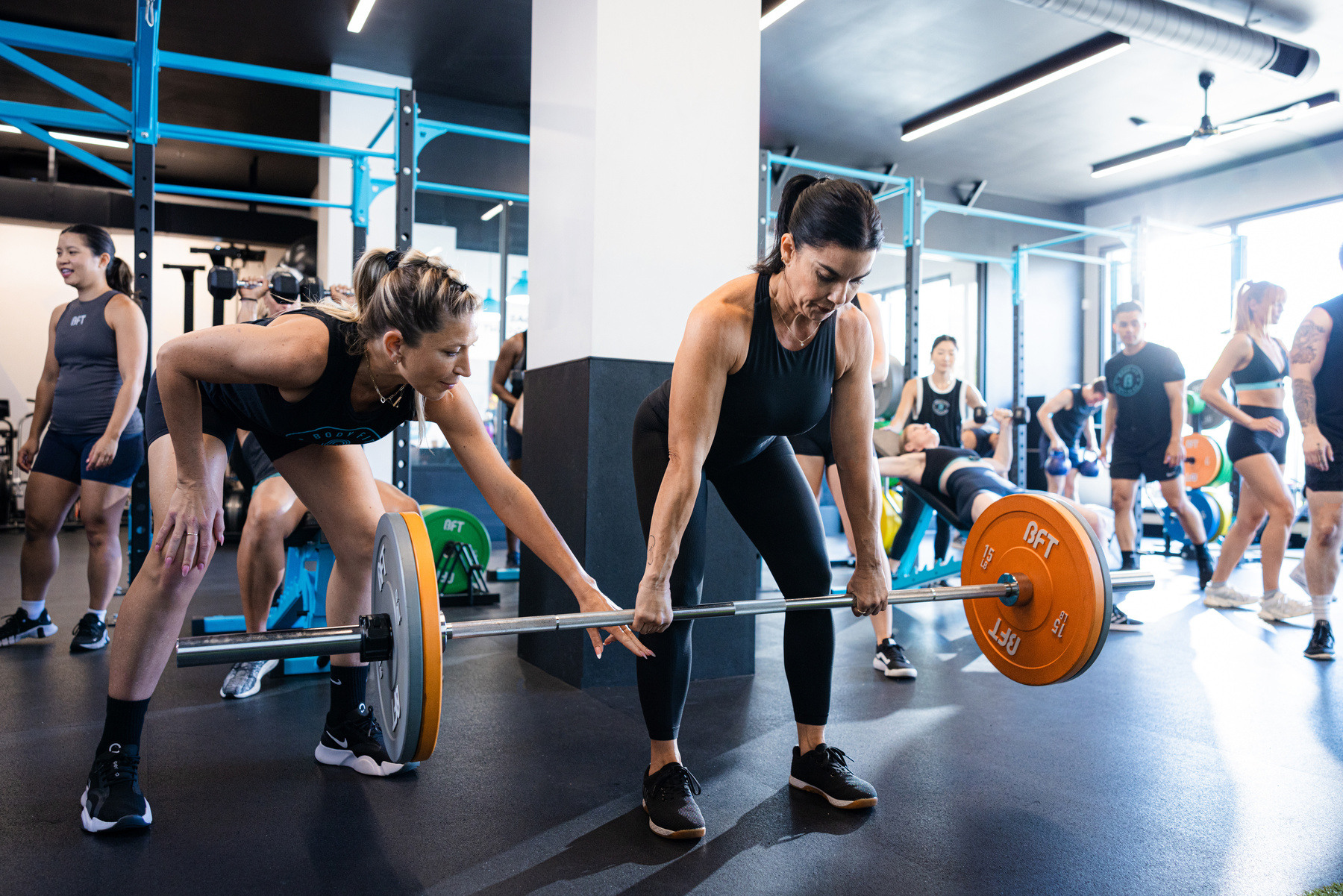 Group session trainee having their form corrected by trainer during deadlift workout