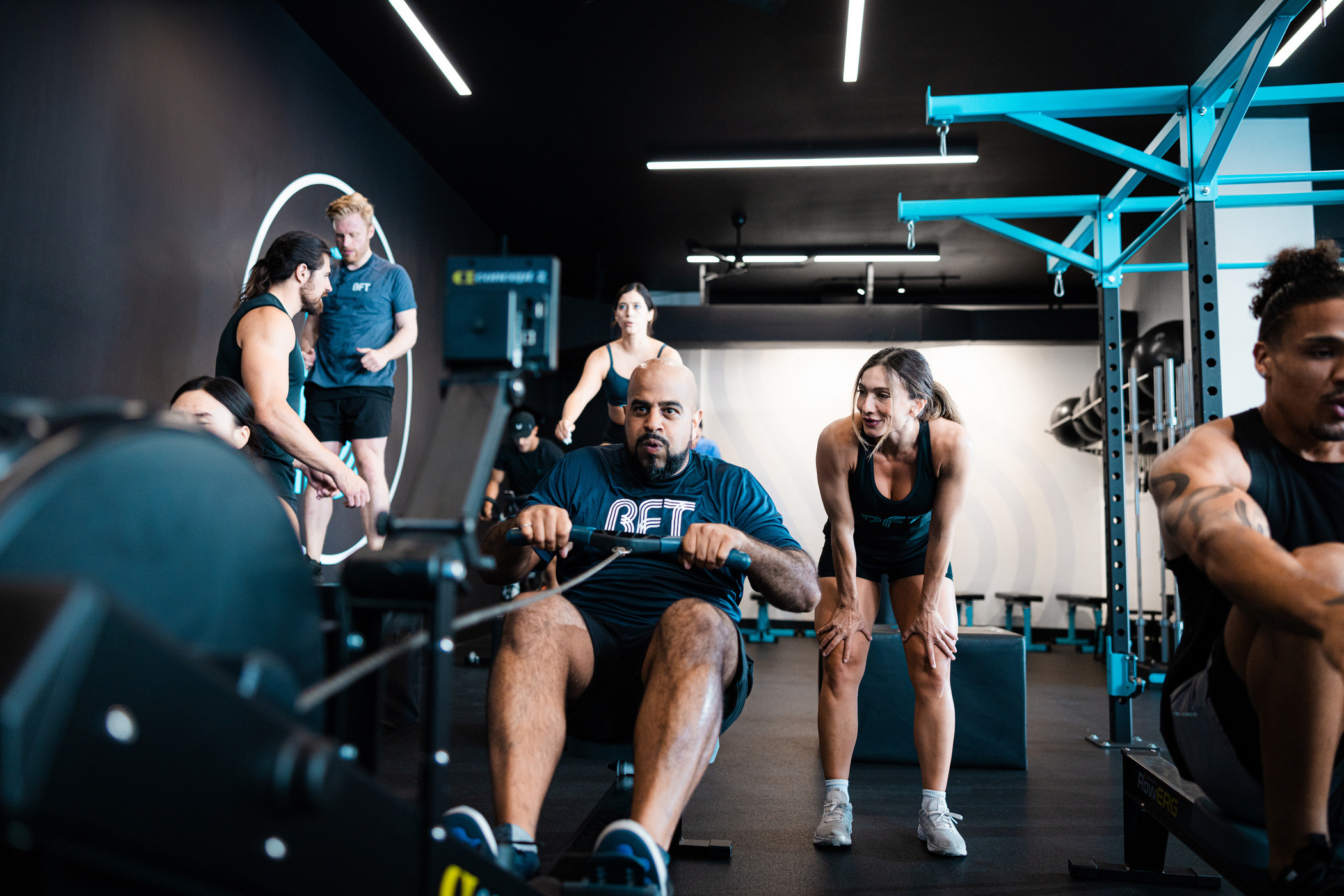 Workout session male attendee using a row machine while his female trainer looks on