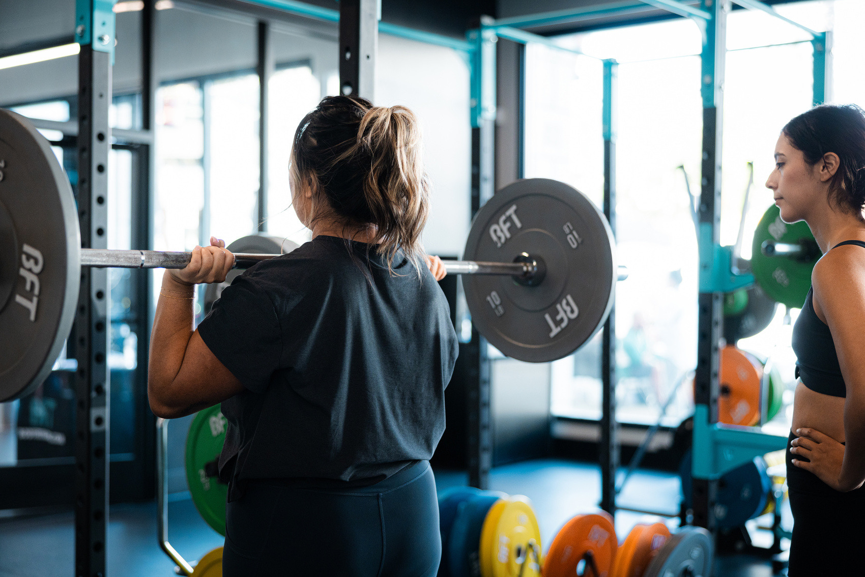 Weight session female attendee demonstrating a barbell overhead press while a trainer looks on