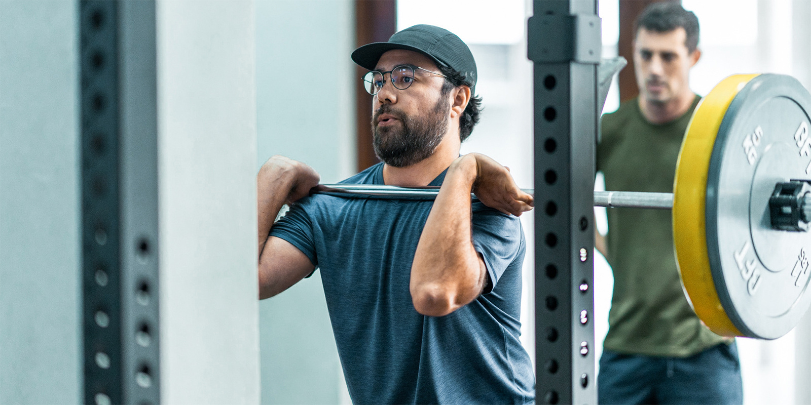 Body Fit Training workout session attendee demonstrating a bar lift with a trainer providing assistance